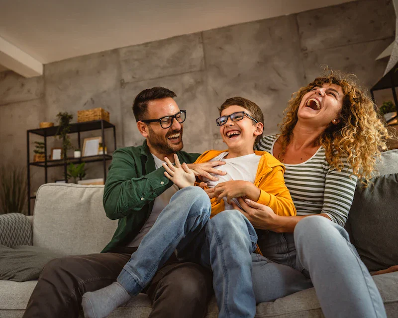A family of three interacts playfully on a cozy couch in a modern living room, surrounded by stylish decor and soft lighting.